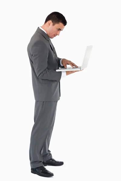 Стоящий бизнесмен, печатающий на своем ноутбуке против белого бэкгра — стоковое фото