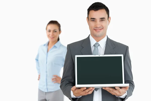 Geschäftsmann präsentiert Laptop mit Geschäftsfrau im Hintergrund — Stockfoto