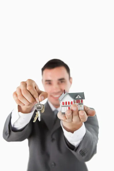 Miniatuur huis en sleutels wordt gepresenteerd door mannelijke onroerende goederenagent — Stockfoto