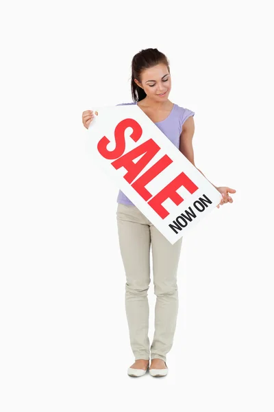 Jovem mulher olhando para o sinal de vendas em suas mãos — Fotografia de Stock