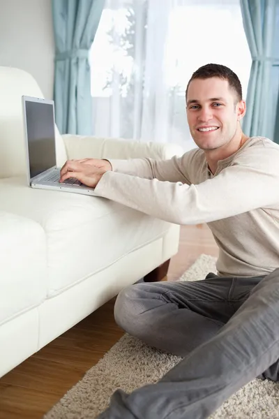 Portrait of a smiling man sitting on a carpet with a laptop — Stock Photo, Image