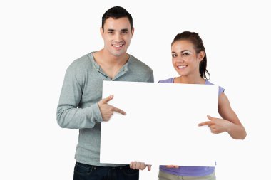 Smiling young couple pointing at sign they are holding clipart