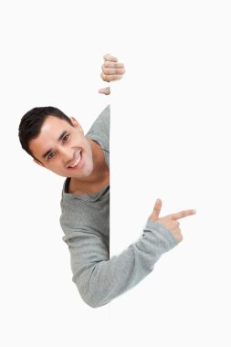 Smiling young male pointing around the corner clipart