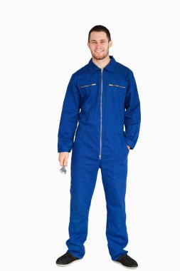 Smiling young mechanic in boiler suit holding a wrench clipart