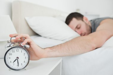 Sleeping young man being awakened by an alarm clock clipart
