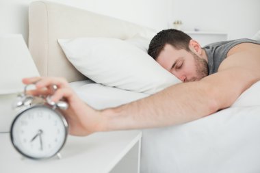 Sleeping handsome man being awakened by an alarm clock clipart