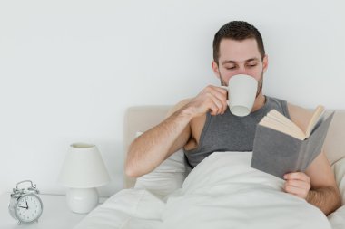 Man reading a book while holding a cup of coffee clipart