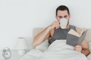 Man reading a novel while holding a cup of coffee clipart