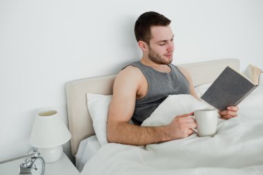 Smiling man reading a novel while having a tea clipart