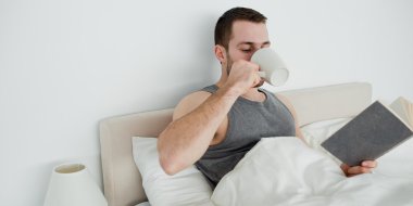 Smiling man reading a novel while drinking a tea clipart