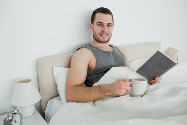 Young man reading a novel while drinking a coffee clipart