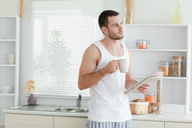 Good looking man drinking coffee while reading the news clipart