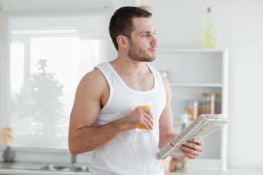 Young man drinking orange juice while reading the news clipart