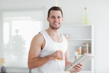 Handsome man drinking orange juice while reading the news clipart