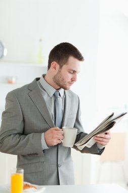 Portrait of a handsome businessman having breakfast while readin clipart