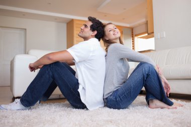 Side view of couple sitting on the floor back-to-back clipart