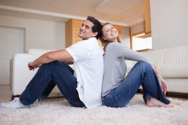 Side view of couple sitting on the carpet back-to-back clipart