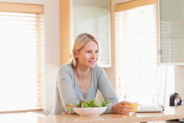 Female with salad and laptop in the kitchen having a glass of or clipart