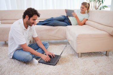 Woman using a tablet computer while her husband is using a lapto clipart
