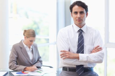 Businessman posing while his colleague is working clipart