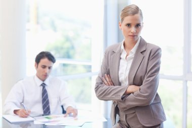 Serious businesswoman posing while her colleague is working clipart