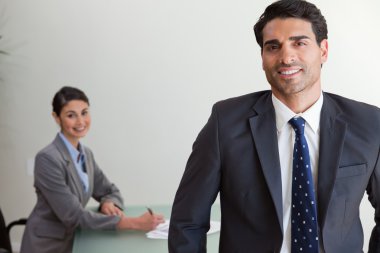 Good looking businessman posing while his colleague is working clipart