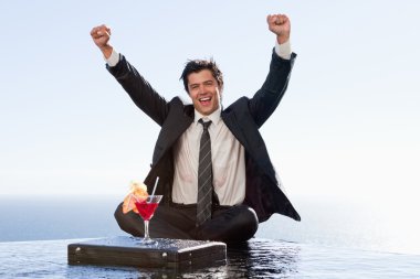 Businessman relaxing with a cocktail and his fists up clipart