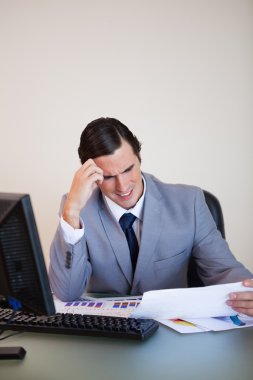 Businessman getting a headache from looking at paperwork clipart