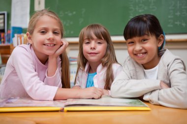 Smiling schoolgirls reading a fairy tale to their classmate clipart