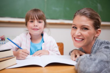 Schoolgirl writing with her teacher clipart