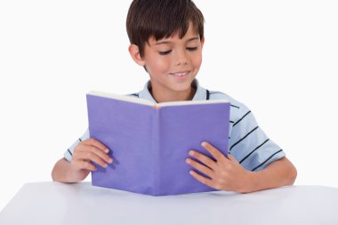 Smiling boy reading a book clipart