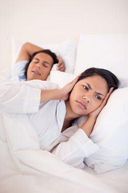 Woman covering her ears to block her boyfriends snoring clipart