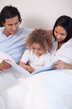 Family sitting on the bed reading a story clipart