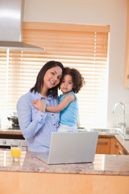 Mother and daughter with laptop in the kitchen clipart