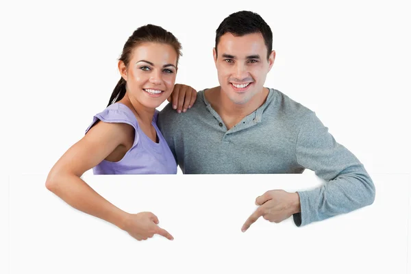 Young couple pointing at advertisement below them — Stock Photo, Image