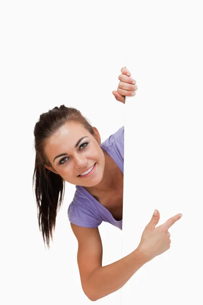 Uśmiechnięta młoda kobieta wskazując za rogiem — Zdjęcie stockowe