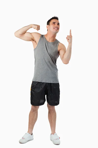Joven macho mostrando sus bíceps mientras señala hacia arriba — Foto de Stock
