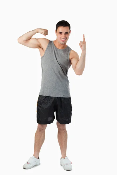 Jovem do sexo masculino apontando para cima enquanto mostra seu bíceps — Fotografia de Stock