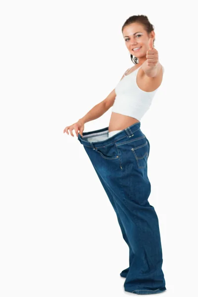 Portrait of a fit woman wearing too large pants with the thumb u — Stock Photo, Image
