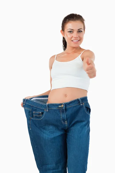 Retrato de una mujer en forma usando pantalones vaqueros demasiado grandes con el pulgar u —  Fotos de Stock
