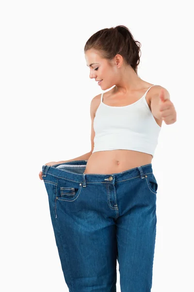 Portrait of a thin woman wearing too large jeans with the thumb — Stock Photo, Image