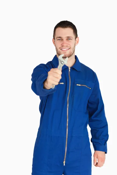 Sorrindo jovem mecânico em terno caldeira mostrando uma chave inglesa — Fotografia de Stock