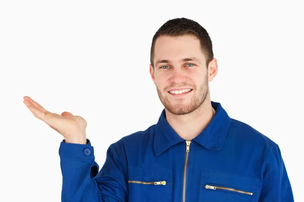 Sonriente joven mecánico presentando algo en su palma — Foto de Stock