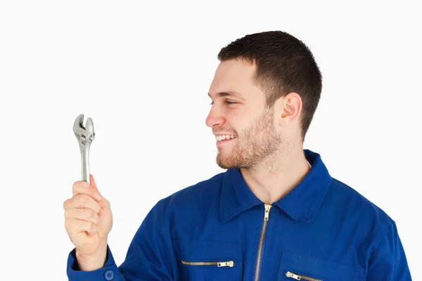 Sorrindo jovem mecânico em terno de caldeira olhando para sua chave inglesa — Fotografia de Stock