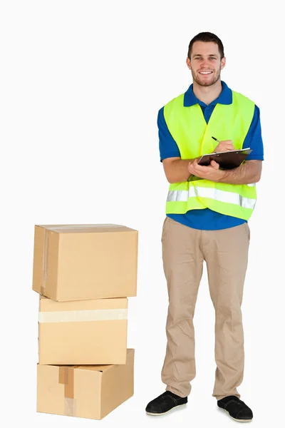 Smiling young delivery man filling in delivery note — Stock Photo, Image