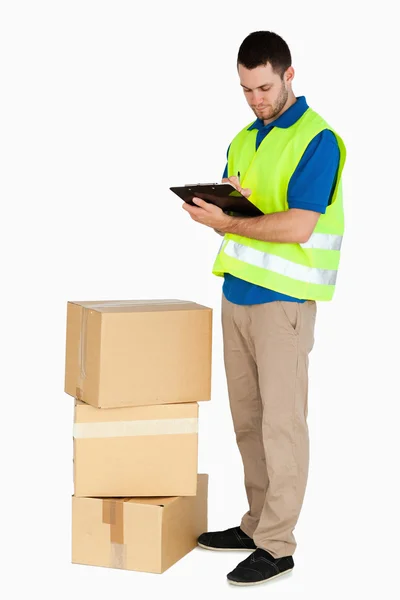 Side view of young delivery man filling in delivery note — Stock Photo, Image