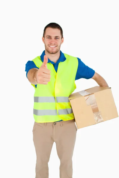 Sorridente giovane uomo di consegna con pacco dando pollice in su — Foto Stock