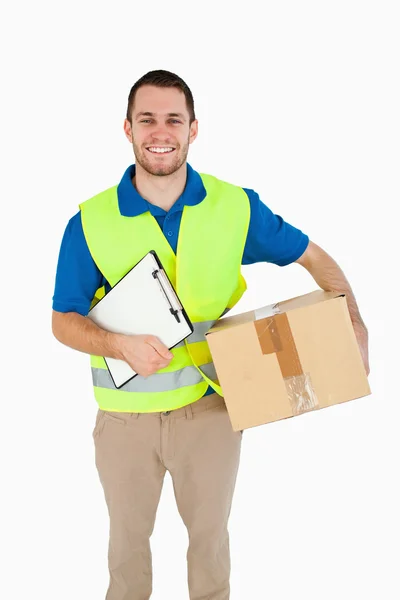 Sorrindo jovem entregador com pacote e nota de entrega — Fotografia de Stock