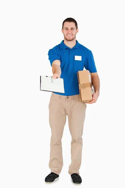 Sonriente joven vendedor con el paquete pidiendo la firma — Foto de Stock