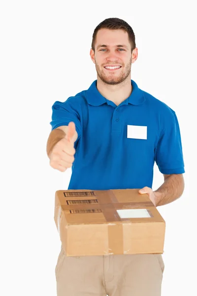 Sorrindo jovem vendedor com pacote dando polegar para cima — Fotografia de Stock